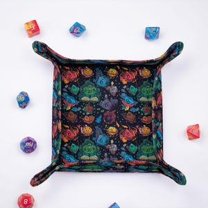 May include: A black dice rolling tray with a colorful design featuring dice, books, and clouds. The tray has a soft, felt-like lining and four corners that fold up to create a secure space for dice.