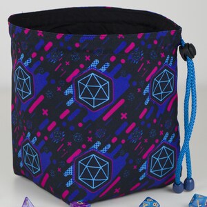 Puede incluir: Bolsa de dados negra con un patr&oacute;n repetido de formas geom&eacute;tricas azules y rosas y un cord&oacute;n azul. El interior de la bolsa es negro. El dise&ntilde;o incluye una gran forma de dado de 20 caras azul. Ideal para guardar dados.