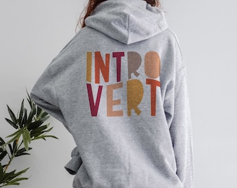 May include: A gray hooded sweatshirt with the word "INTROVERT" printed on the back in colorful block letters. The letters are in shades of red, orange, yellow, and brown.