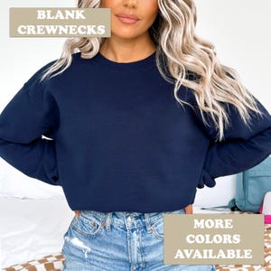 May include: A navy blue crewneck sweatshirt. The text "BLANK CREWNECKS" is in the top left corner of the image. The text "MORE COLORS AVAILABLE" is in the bottom right corner of the image.