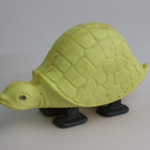Op de afbeelding: Een lichtgroene plastic speelgoed schildpad met zwarte wielen. De schildpad heeft een getextureerde schild en een gedetailleerd gezicht.