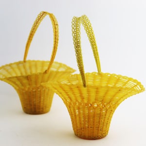 May include: Two yellow woven baskets with handles. The baskets are made of a thin, flexible material and have a scalloped edge.