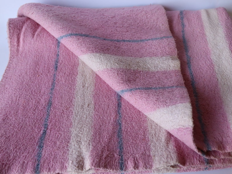 Puede incluir: Una manta de rayas rosa y blancas con rayas azules. La manta est&aacute; doblada por la mitad y tiene una textura suave y peluda.