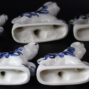 May include: A collection of white ceramic figurines with blue floral designs. The figurines are in a reclining pose, with a rectangular base and a hole. The background is black.