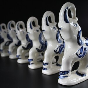 May include: A row of white ceramic elephant figurines with blue floral designs. The elephants are standing on a black surface. The figurines are in a line, with the closest one in sharp focus.