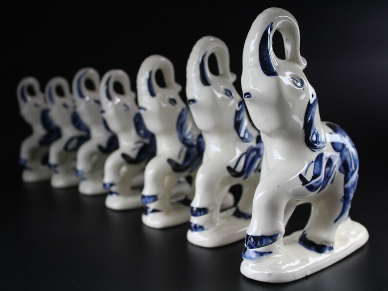 May include: A row of white ceramic elephant figurines with blue floral designs. The elephants are standing on a black surface. The figurines are in a line, with the closest one in sharp focus.