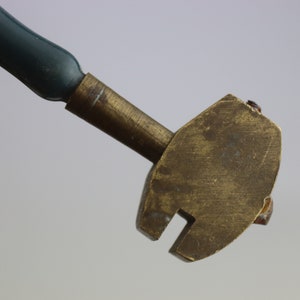 May include: A brass glass cutter with a green plastic handle. The cutter has a sharp wheel and a small lever to adjust the depth of the cut.