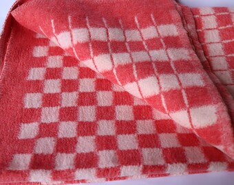 Peut inclure: Une couverture pliée à carreaux rouges et blancs. La couverture a une texture douce et floue avec un motif répétitif de carrés rouges et blancs. Les bords sont finis avec une bordure cousue.
