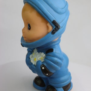 K&ouml;nnte beinhalten: Ein blauer Spielzeug-Astronaut aus Gummi, der einen Strau&szlig; wei&szlig;er Blumen h&auml;lt. Der Astronaut tr&auml;gt einen Helm und hat ein freundliches Gesicht.