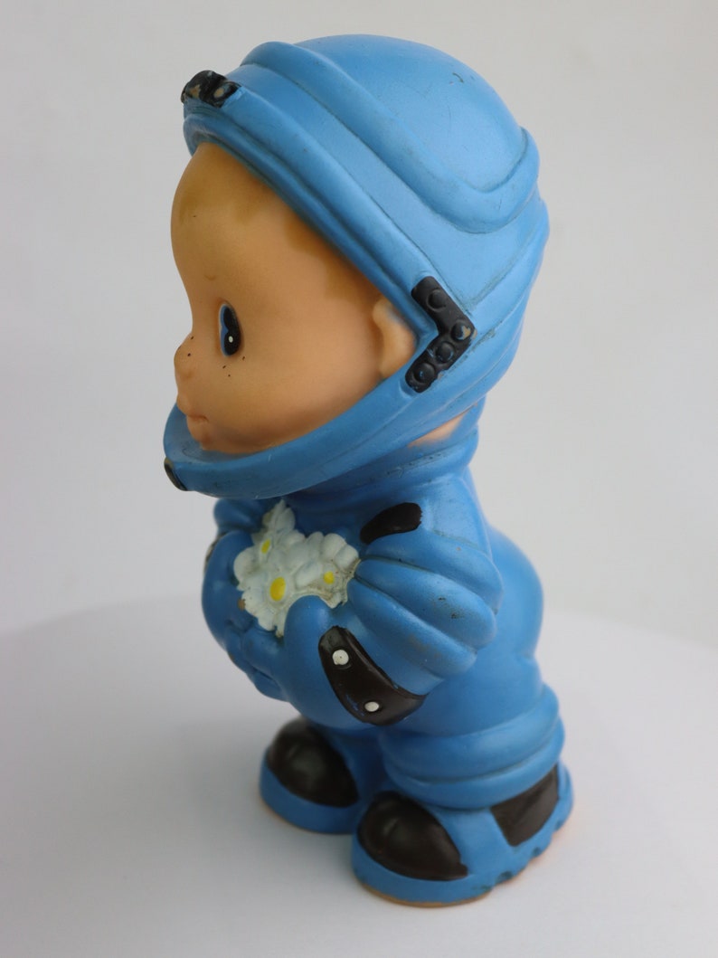 K&ouml;nnte beinhalten: Ein blauer Spielzeug-Astronaut aus Gummi, der einen Strau&szlig; wei&szlig;er Blumen h&auml;lt. Der Astronaut tr&auml;gt einen Helm und hat ein freundliches Gesicht.