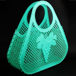 May include: A turquoise plastic tote bag with a grape design. The bag has a mesh design and a handle.