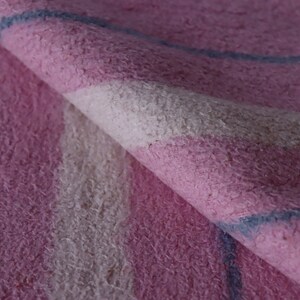Puede incluir: Primer plano de una tela de rayas rosa y blancas con una raya azul. La tela tiene una textura peluda.