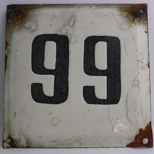 May include: A white metal sign with black numbers, the number 99 is displayed on the sign. The sign has a rusty edge and is slightly weathered.