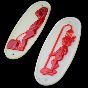 May include: Two white oval-shaped signs with red figures. The sign on the left shows a figure urinating into a bucket. The sign on the right shows a figure holding a shower head.