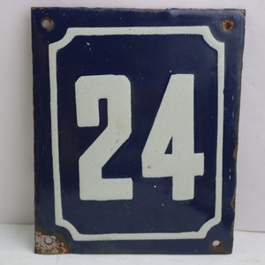 May include: A blue enamel house number sign with white painted numerals, the number 24, on a white background.