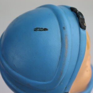 K&ouml;nnte beinhalten: Ein blauer Plastikhelm mit einem schwarzen Riemen und einem kleinen schwarzen Detail an der Seite. Der Helm weist Gebrauchsspuren auf.