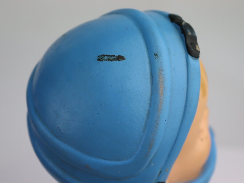 K&ouml;nnte beinhalten: Ein blauer Plastikhelm mit einem schwarzen Riemen und einem kleinen schwarzen Detail an der Seite. Der Helm weist Gebrauchsspuren auf.