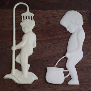 May include: Two white ceramic figurines of people, one holding a shower head and the other holding a bucket.