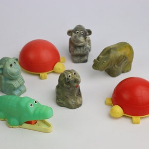 Puede incluir: Un conjunto de seis figuras de animales, que incluyen un cocodrilo verde, una tortuga verde, una tortuga roja, un mono gris, un perro gris y un rinoceronte verde. Las figuras están hechas de plástico y piedra.