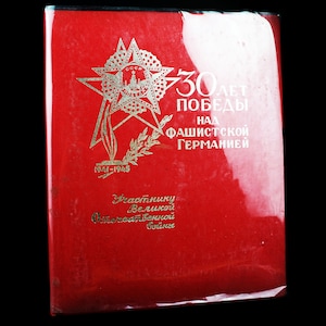 May include: A red booklet with gold lettering commemorating the 30th anniversary of the victory over fascist Germany. The cover features a gold star with a red star inside, and the text "30 лет победы над фашистской Германией (1941-1945)" is printed in gold.