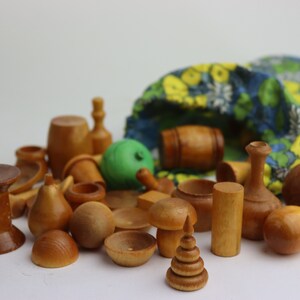 Könnte beinhalten: Eine Sammlung von Holzspielzeug in verschiedenen Formen und Größen, darunter eine Birne, ein Pilz, eine Spule, eine Vase und ein Fass. Die Teile liegen auf einer weißen Oberfläche verstreut und fallen teilweise aus einer Stofftasche mit Blumenmuster.