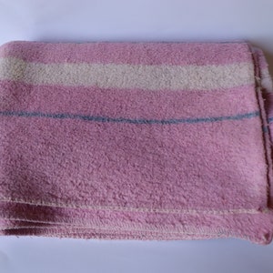 Puede incluir: Una manta de rayas rosa y blancas con una raya azul. La manta est&aacute; doblada y parece estar hecha de un material suave y peludo.