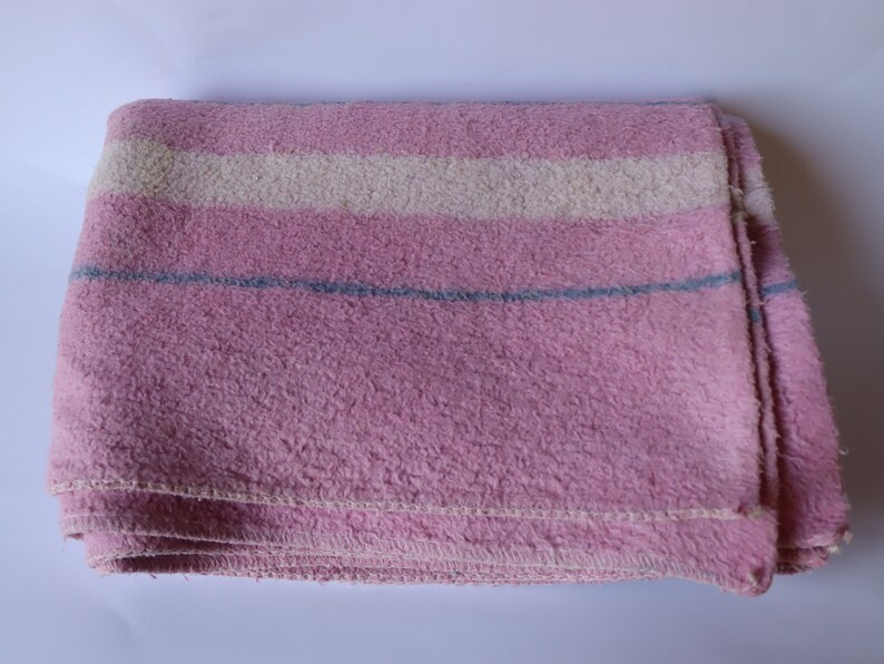 Puede incluir: Una manta de rayas rosa y blancas con una raya azul. La manta est&aacute; doblada y parece estar hecha de un material suave y peludo.