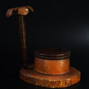 May include: A wooden box with a lid, carved to resemble a palm tree. The box is made of light and dark wood and sits on a wooden base.