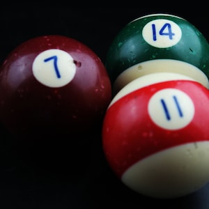 May include: Three billiard balls, one red with the number 11, one green with the number 14, and one maroon with the number 7.