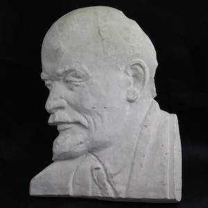 May include: A white plaster bust of a man with a beard and mustache. The bust is in profile, with the man's head turned to the left. The bust is a simple, realistic depiction of the man's features.