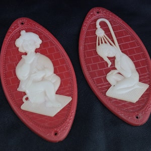 May include: Two red oval-shaped signs with white raised relief images of people. One sign shows a person sitting on a toilet and the other shows a person taking a shower.