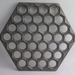 May include: Hexagonal metal dumpling maker with a honeycomb design. The gray mold features 37 circular openings for shaping dumplings. This kitchen tool is designed to create uniform dumplings.