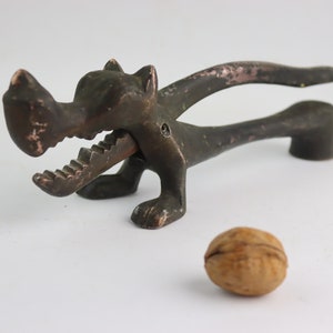 Può includere: Un tradizionale schiaccianoci in metallo a forma di lupo con una noce marrone rotta di fronte.