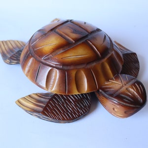 May include: A wooden turtle figurine with a brown and yellow finish. The turtle's shell is carved with intricate details and the legs are outstretched.