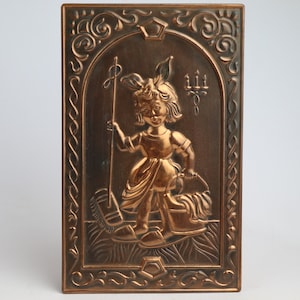 Pode incluir: Uma placa de parede de cobre com uma moldura ornamentada que representa uma menina com um vestido segurando um pau e uma cesta. A placa tem um design em relevo.