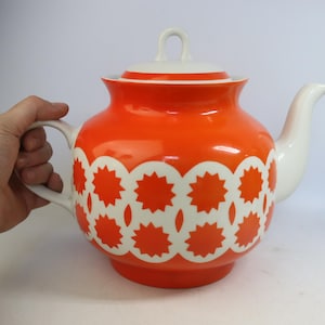 Könnte beinhalten: Eine leuchtend orangefarbene Teekanne mit weißem Deckel, Griff und Ausguss. Die Teekanne hat ein sich wiederholendes weißes Sternmuster um den Körper. Die Teekanne ist im Vintage-Stil und aus Keramik gefertigt.