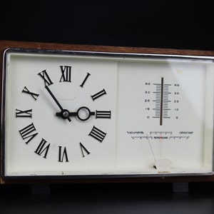 May include: A vintage wooden framed clock and thermometer with Roman numeral clock face and a Fahrenheit scale thermometer. The clock face is white with black hands and black Roman numerals. The thermometer is white with a black needle and black markings.