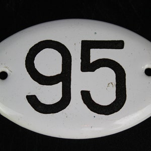 May include: White oval-shaped porcelain sign with black painted number 95. The sign has two small holes on either side.