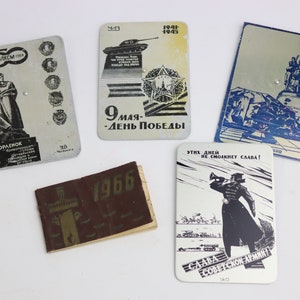 May include: A collection of vintage metal cards and a small booklet. The cards feature illustrations of monuments, military figures, and tanks, with text in Russian. The booklet is brown with the year 1966 printed on the cover. The cards have a silver and blue color scheme.