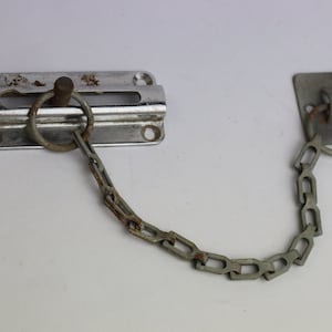 May include: A silver door chain with a metal latch and a ring on each end. The chain is attached to the latch with a metal ring.