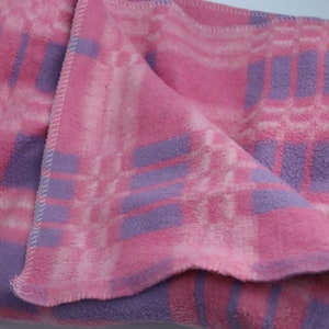 Puede incluir: Una manta de franela a cuadros rosa y morado con una textura suave y peluda.