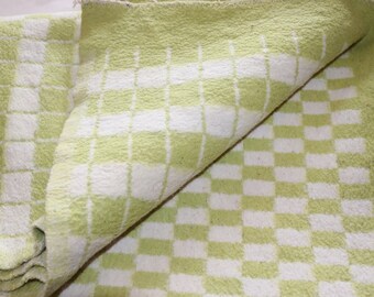 Peut inclure: Un tissu à carreaux vert et blanc avec une texture douce et duveteuse. Le tissu est plié en deux, révélant le motif à carreaux.