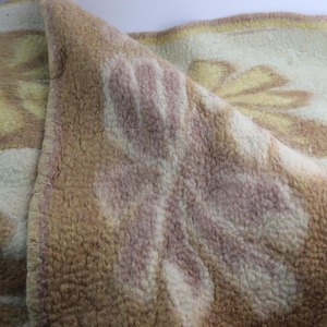 Puede incluir: Primer plano de una alfombra texturizada con un diseño floral. La alfombra presenta un fondo crema con diseños florales marrones, amarillos y rosas. La alfombra está doblada, revelando el reverso con un patrón similar.