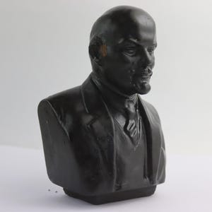 May include: A black bust sculpture of a man in a suit and tie. The sculpture is a detailed representation of a historical figure, with a focus on the face and upper body. The bust is set against a plain white background.
