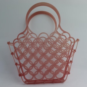 May include: A pink plastic woven tote bag with a single handle. The bag is made of a lattice pattern of interlocking circles.