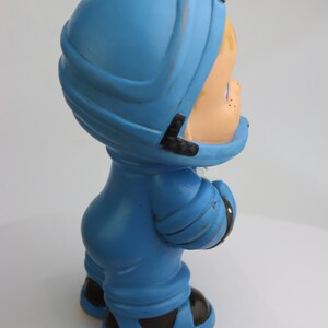 K&ouml;nnte beinhalten: Eine blaue Plastikfigur eines Kindes, das einen Helm und einen blauen Overall tr&auml;gt. Die Figur h&auml;lt ein wei&szlig;es Objekt in der rechten Hand.