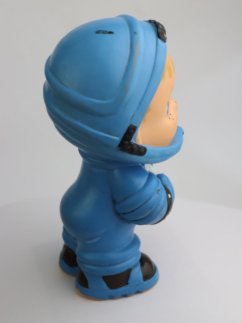 K&ouml;nnte beinhalten: Eine blaue Plastikfigur eines Kindes, das einen Helm und einen blauen Overall tr&auml;gt. Die Figur h&auml;lt ein wei&szlig;es Objekt in der rechten Hand.