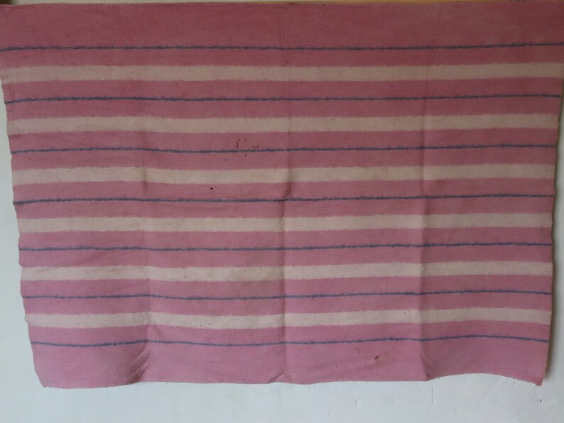 Puede incluir: Una manta de rayas rosa y blancas con textura tejida. La manta tiene un aspecto descolorido y est&aacute; hecha de lana.
