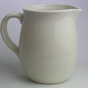 May include: A white ceramic jug with a rounded body and a handle. The jug is empty and has a smooth, glossy finish.