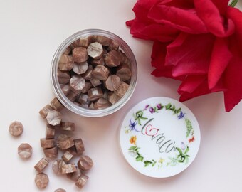 May include: A clear jar filled with brown wax beads, scattered wax beads, and a lid with the word "love" surrounded by a floral wreath. A vibrant red rose is also in the image.
